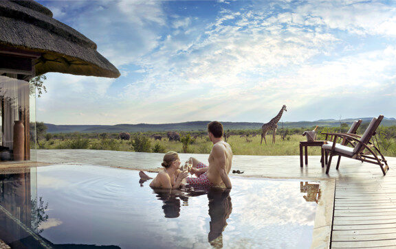 Couple dans une piscine de lodge face à une girafe, réserve de Madikwe, Afrique du Sud