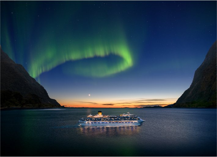 Un navire de Costa illuminé sur un fjord à la tombée de la nuit, sous un arc d’aurore boréale verte
