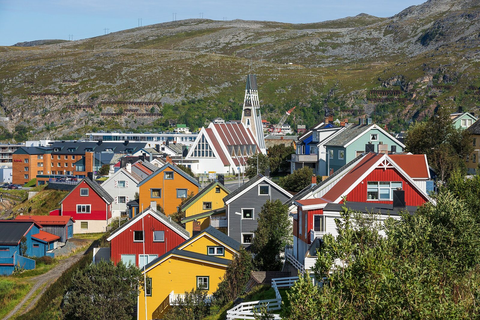 Maisons de bois rouges, jaunes et bleues sur les hauteurs de Hammerfest, avec l’église blanche au fond
