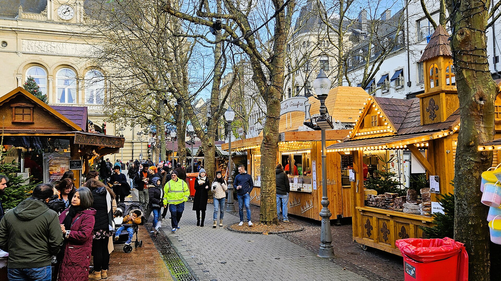 Chalets en bois du marché de Noël de Luxembourg-Ville et promeneurs dans une rue pavée