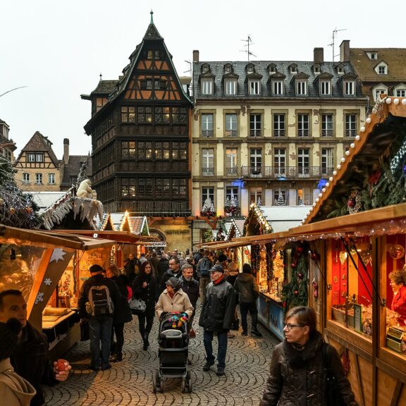 Allée de chalets du marché de Noël de Strasbourg devant la maison Kammerzell, avec des promeneurs