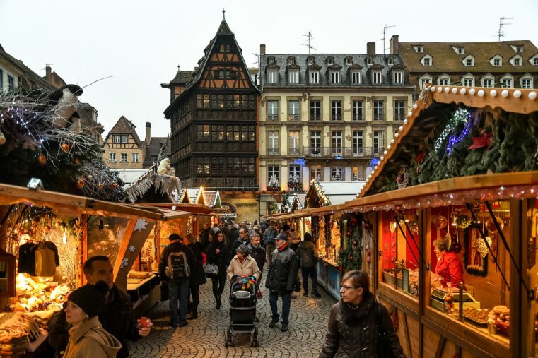 Allée de chalets du marché de Noël de Strasbourg devant la maison Kammerzell, avec des promeneurs