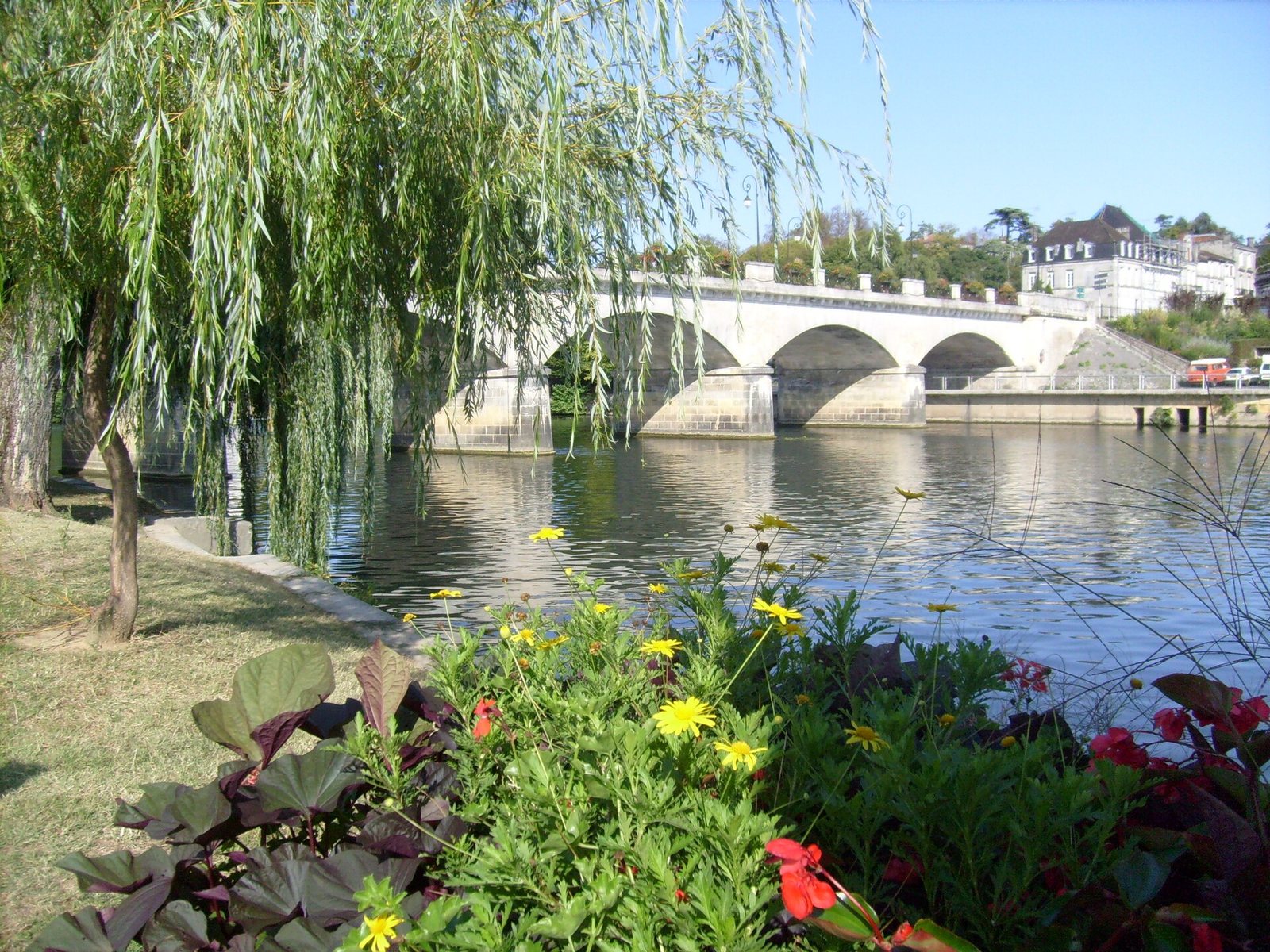 Les quais de la Charente à Cognac, un pont de pierre à trois arches derrière un saule et des massifs de fleurs