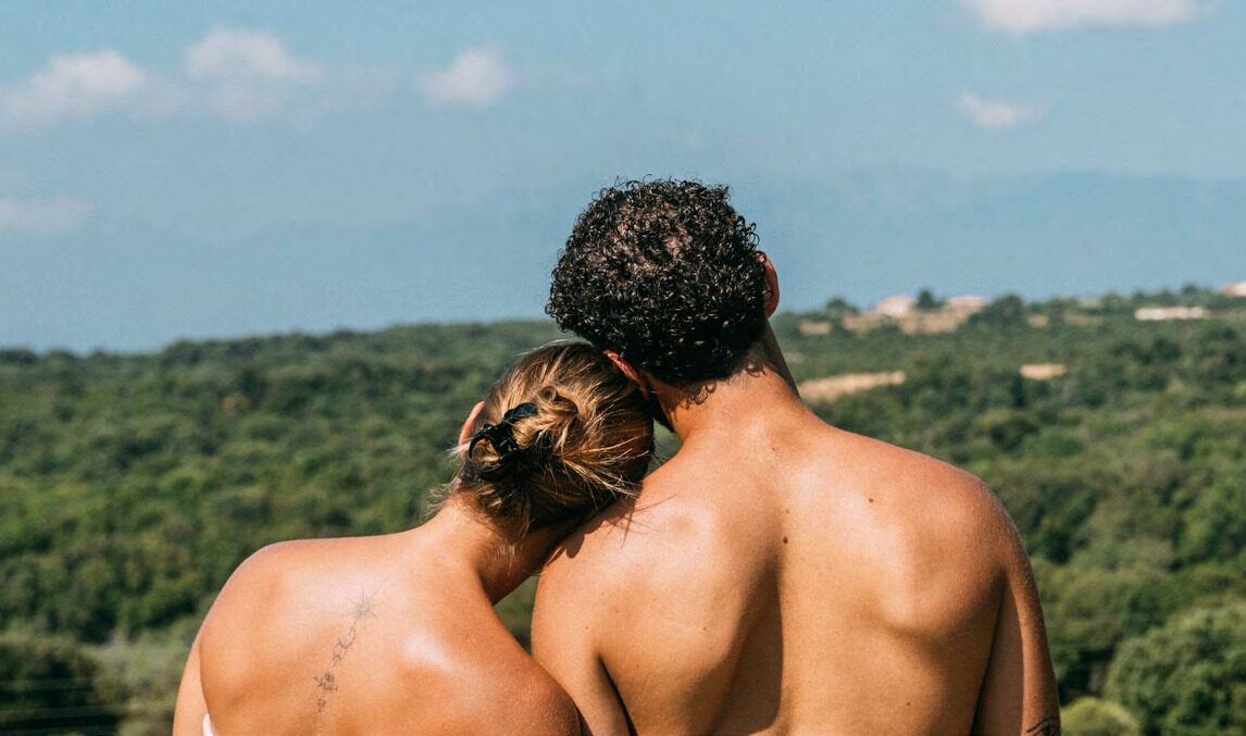 Couple naturiste de dos face à un paysage de collines boisées et de montagnes