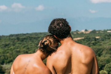 Couple naturiste de dos face à un paysage de collines boisées et de montagnes