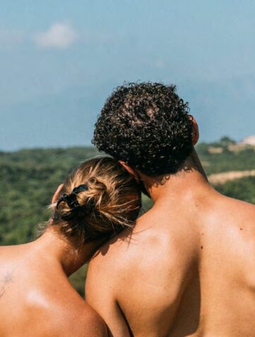 Couple naturiste de dos face à un paysage de collines boisées et de montagnes