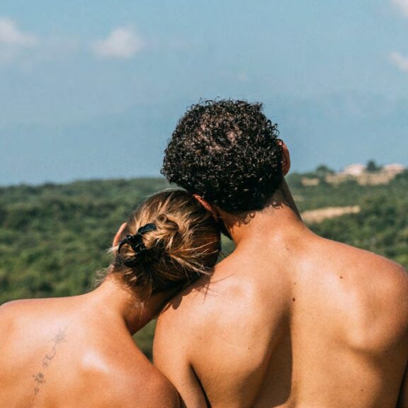 Couple naturiste de dos face à un paysage de collines boisées et de montagnes