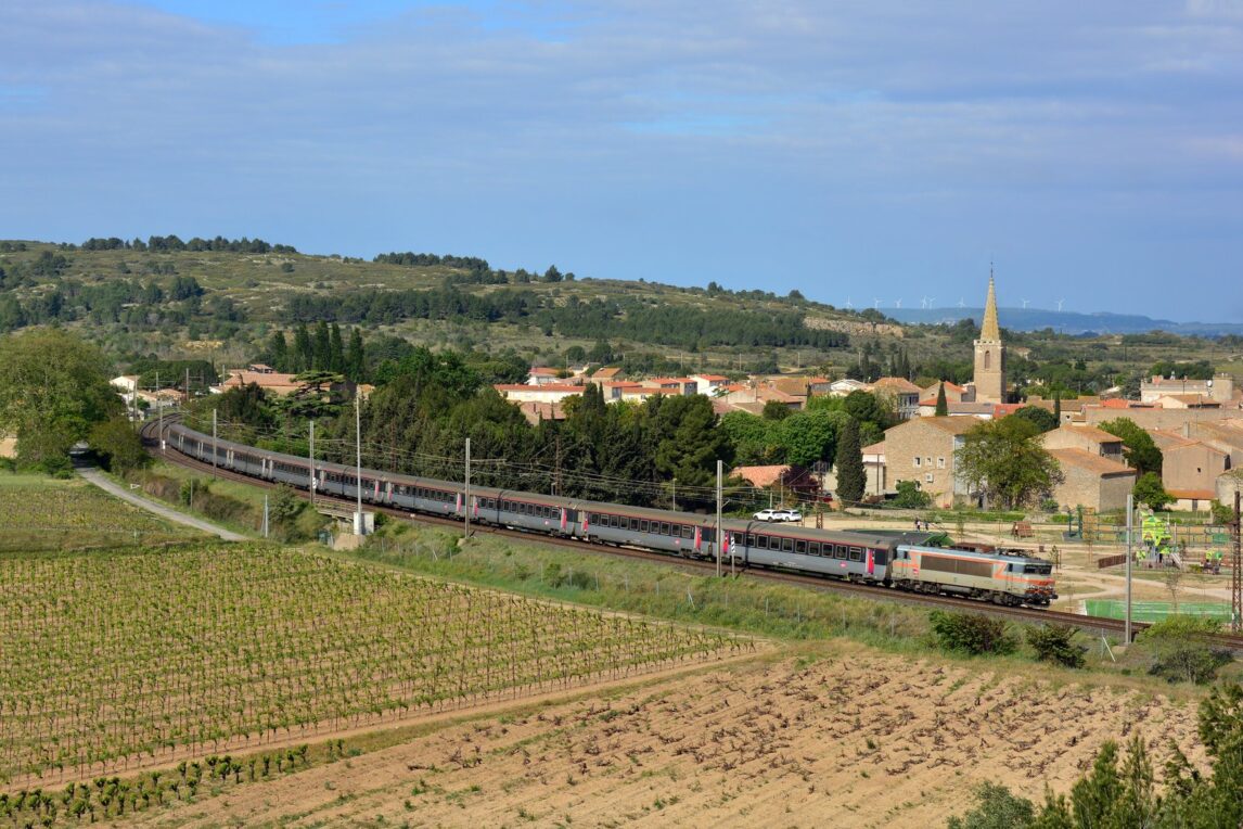 Train Intercités Bordeaux-Marseille tracté par une locomotive grise et orange, entre les vignes et le village de Névian, près de Narbonne