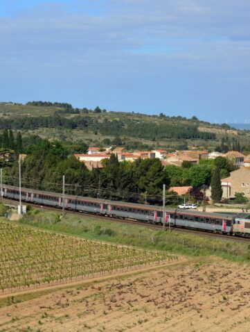 Train Intercités Bordeaux-Marseille tracté par une locomotive grise et orange, entre les vignes et le village de Névian, près de Narbonne