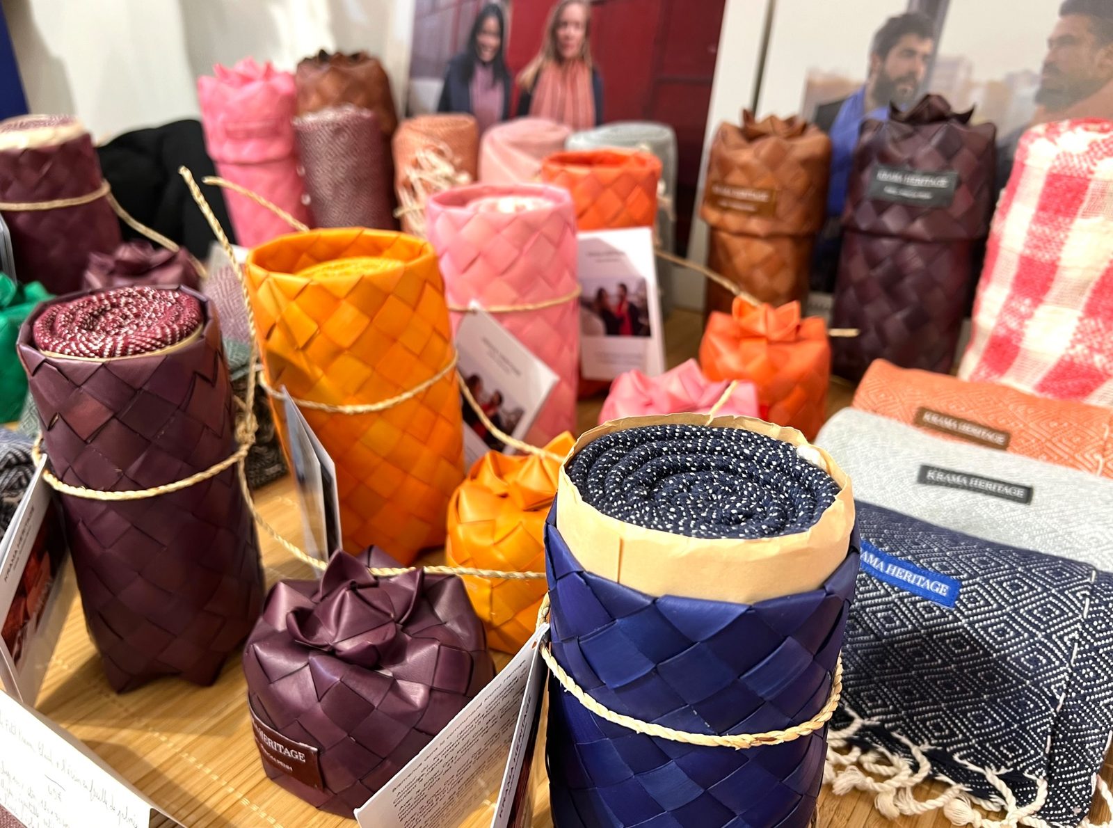 Écrins en feuille de palmier tressée de toutes les couleurs, orange, rose, prune et bleu, exposés sur une table avec des kramas roulés.