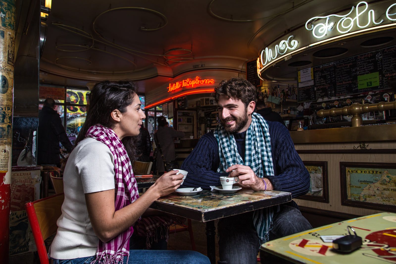Un couple attablé dans un café parisien, chacun porte un Grand Krama Campagnard à carreaux.
