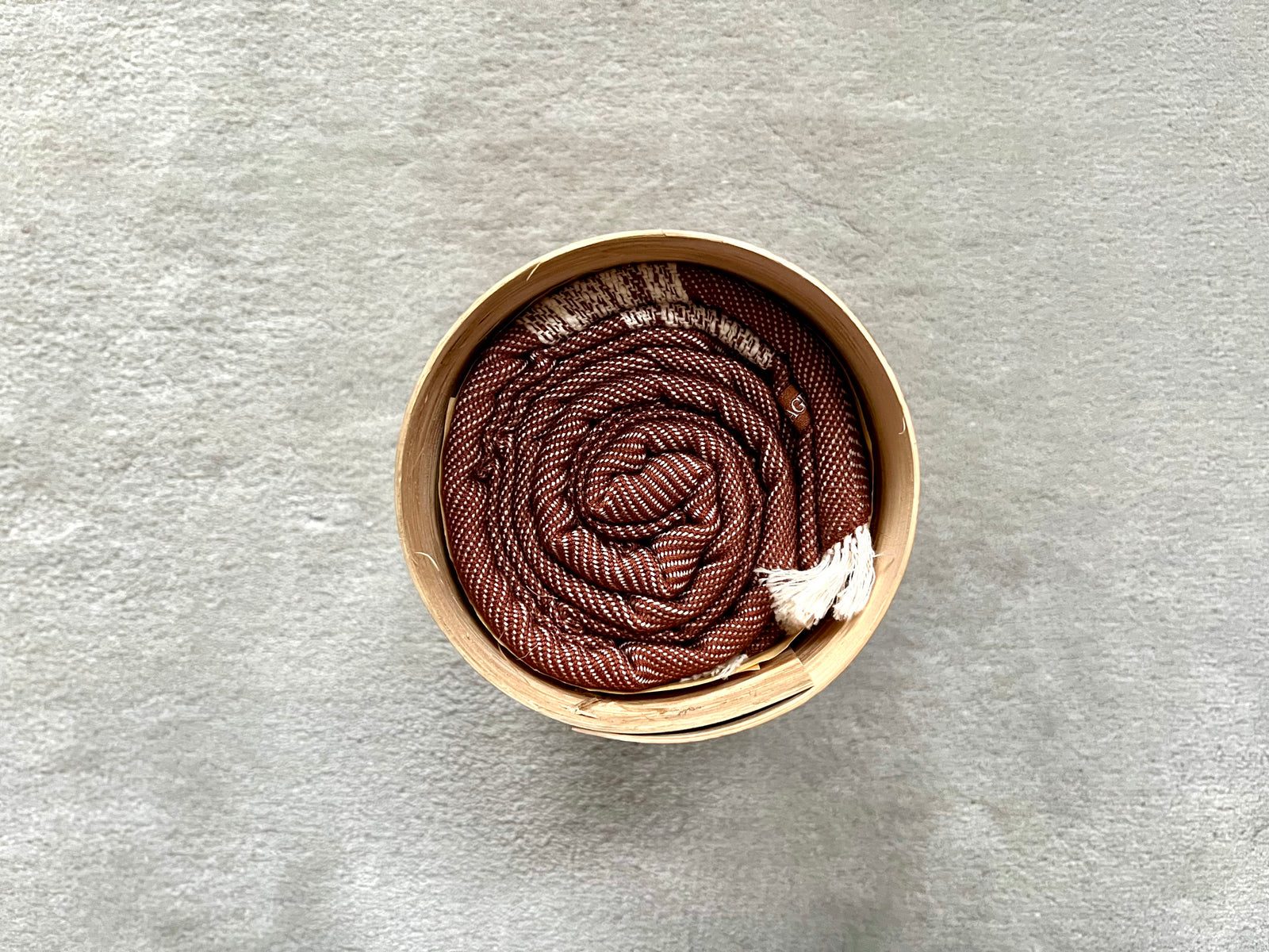 Grand Krama Doux marron roulé dans son écrin rond en écorce de palmier, vu du dessus.