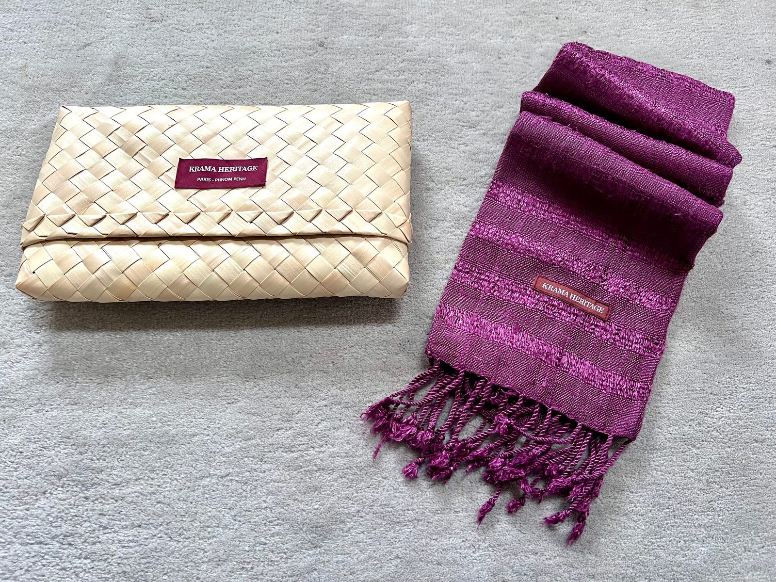 Krama Brut Ondelé en soie sauvage prune, à côté de sa pochette en feuille de palmier tressée.