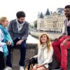 Quatre amis assis sur les quais de Seine face à la Conciergerie, écharpes Krama Heritage à carreaux et à rayures autour du cou.