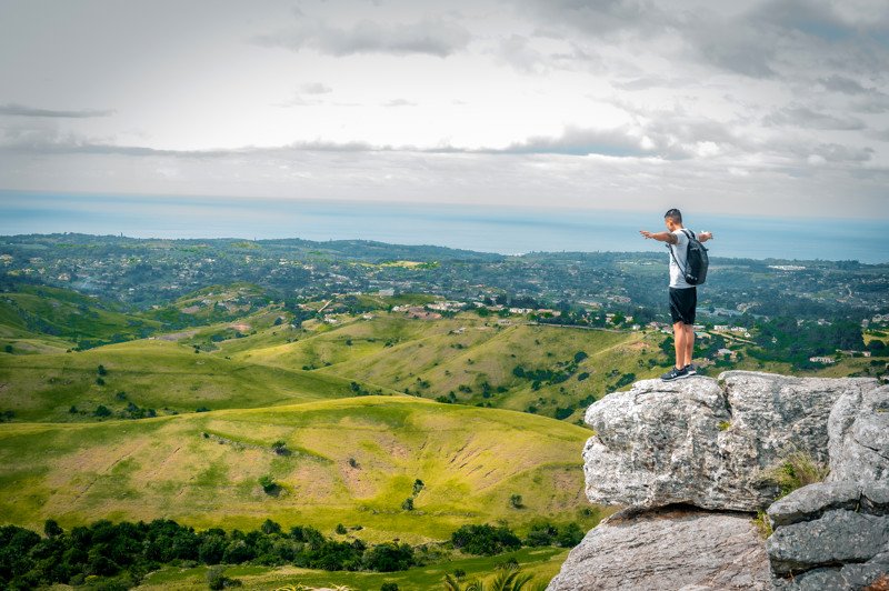 Randonneur sur un rocher face aux collines verdoyantes du KwaZulu-Natal