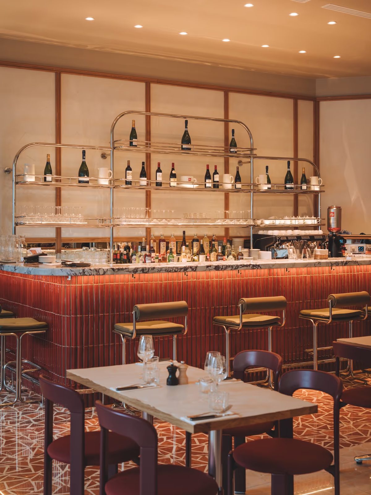 Bar central rouge de Maison Mayane à Porte Maillot, étagères de bouteilles, tabourets et tables de bistrot.