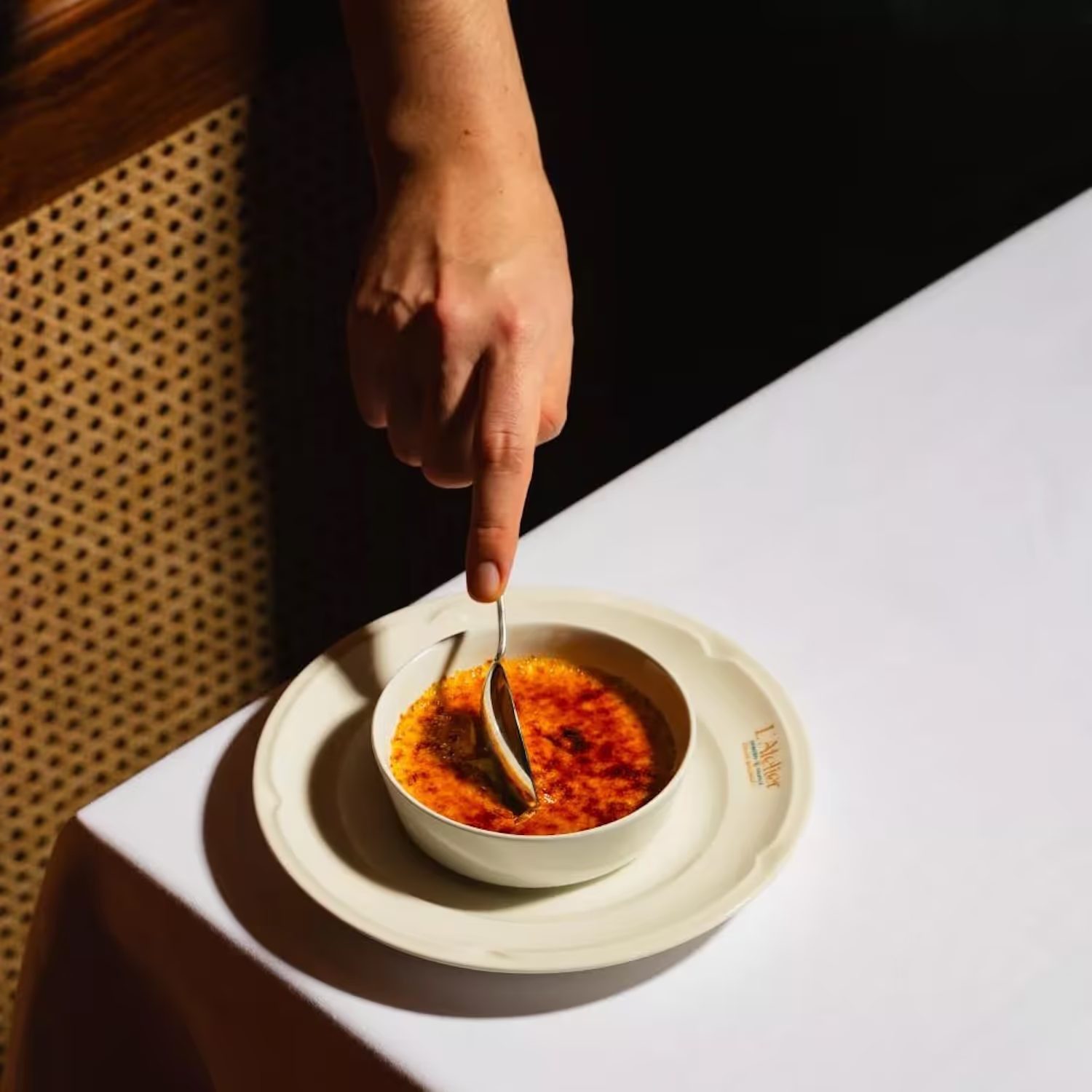 Cuillère plongée dans une crème brûlée caramélisée, sur une table blanche.