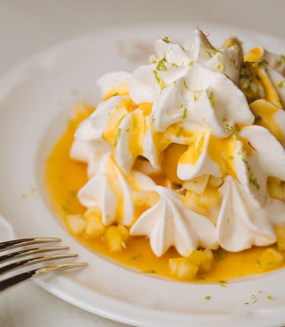 Pavlova garnie de meringue, de fruits jaunes et de zeste de citron vert.