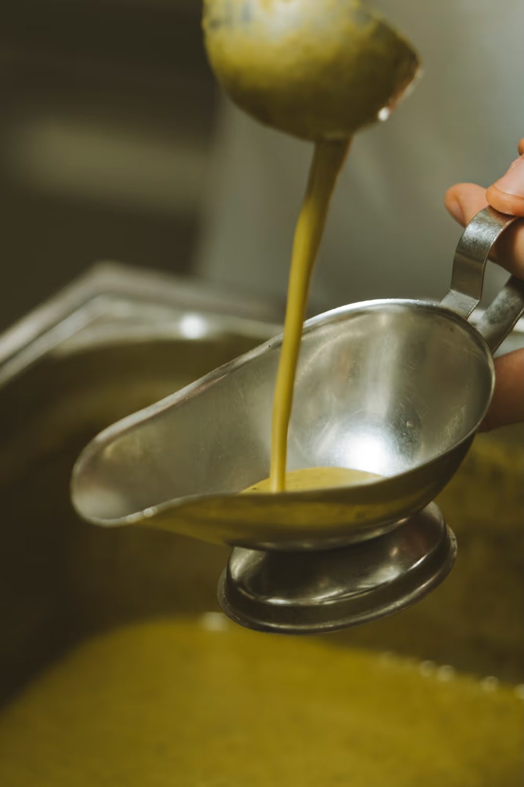 Louche versant la sauce signature verte et dorée dans une saucière en métal.