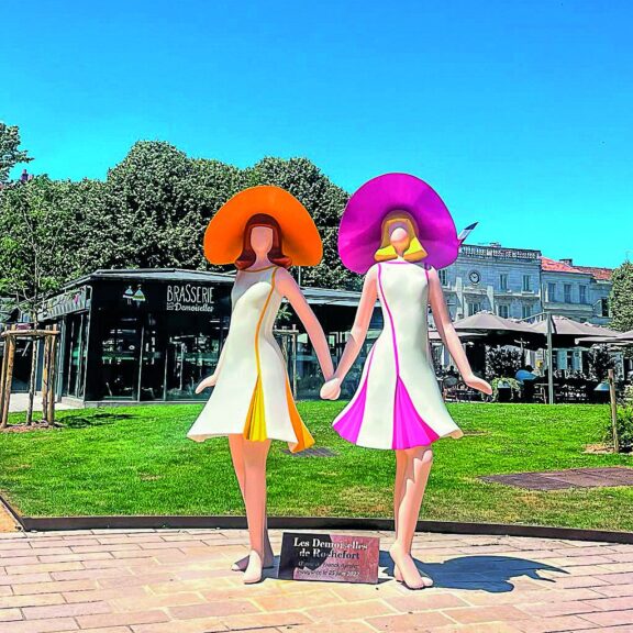 Sculpture des Demoiselles de Rochefort aux chapeaux orange et rose, sur la place Colbert